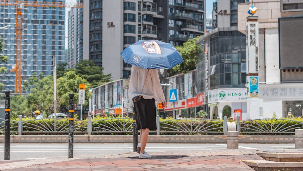 woman in black skirt holding blue umbrella walking on sidewalk during daytime