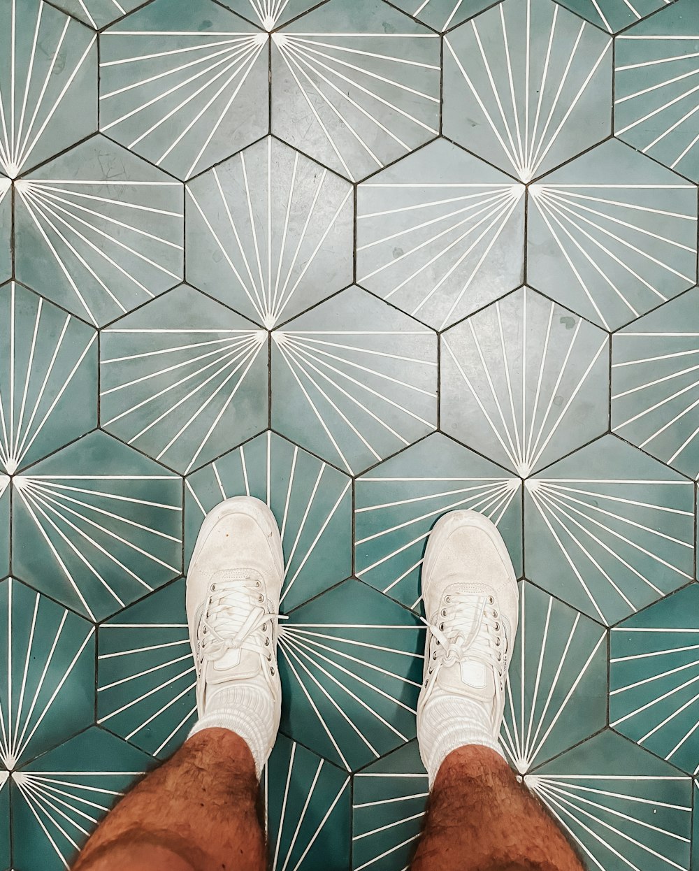 person wearing white shoes standing on white and brown floor tiles