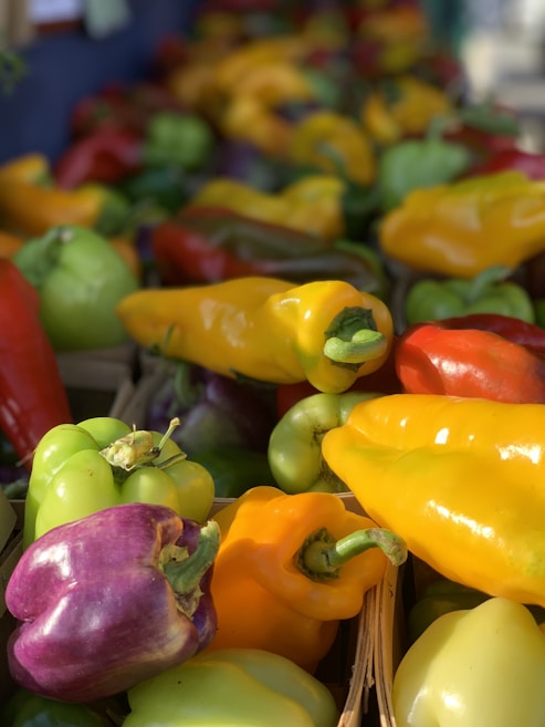 A colorful assortment of bell peppers displayed in various shades, including yellow, red, green, and purple, with a focus on the fresh texture and vibrant hues of the vegetables.