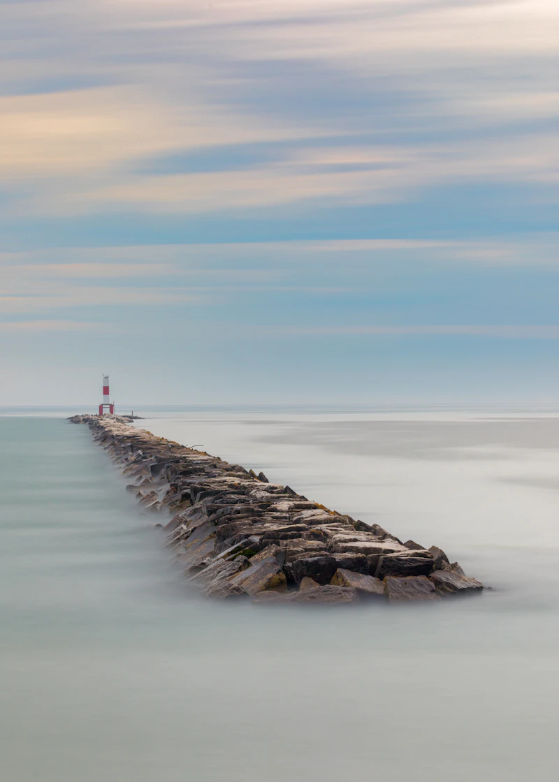 A small lighthouse at the end of a breakwater on glassy water
