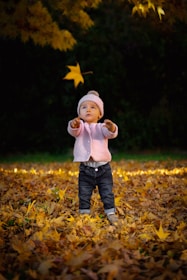 A little girl twirling in a cozy, hand-knit sweater from minimooses, surrounded by autumn leaves.