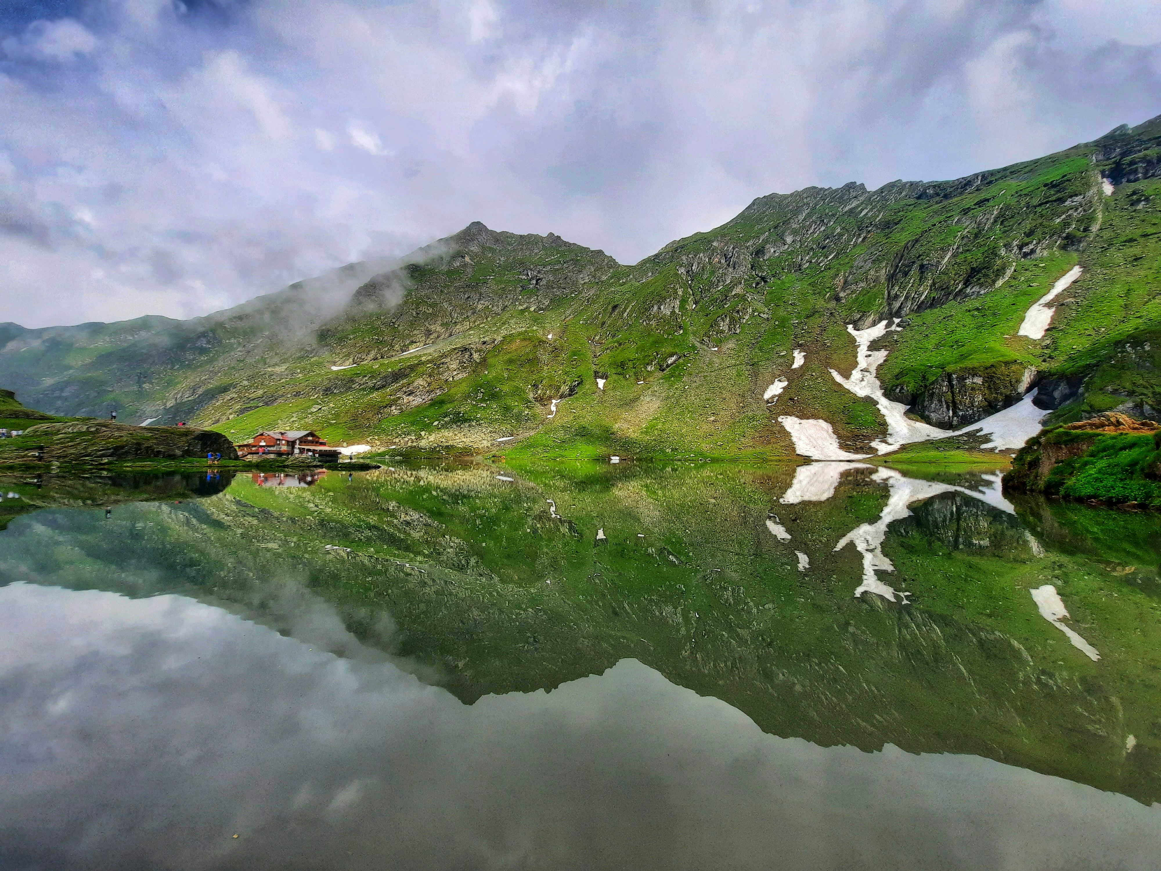 Grüner Berg am See tagsüber unter bewölktem Himmel