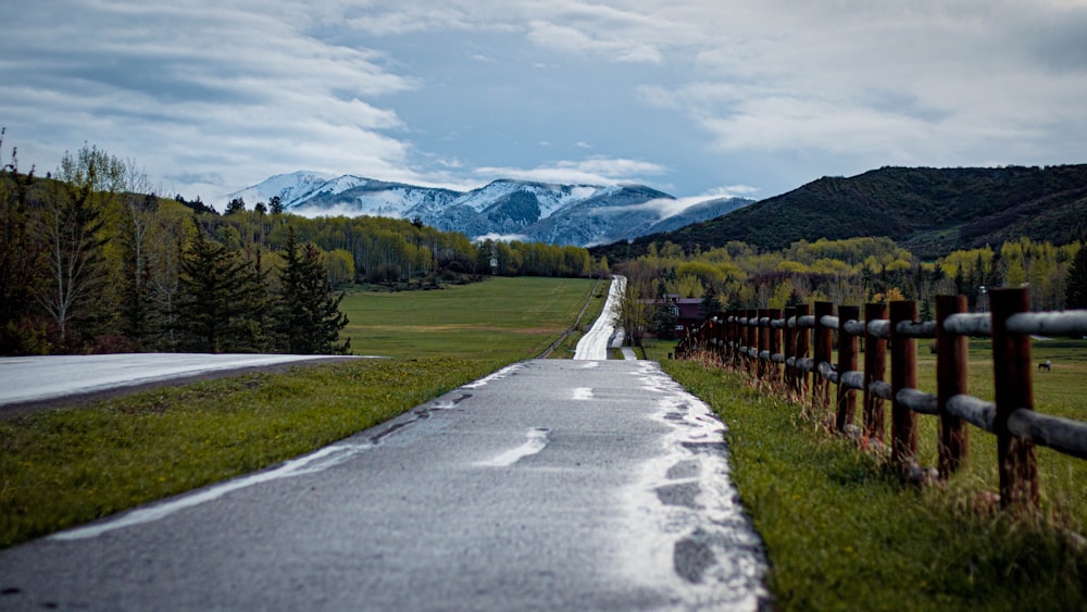 gray concrete road between green grass field and trees under white clouds and blue sky during