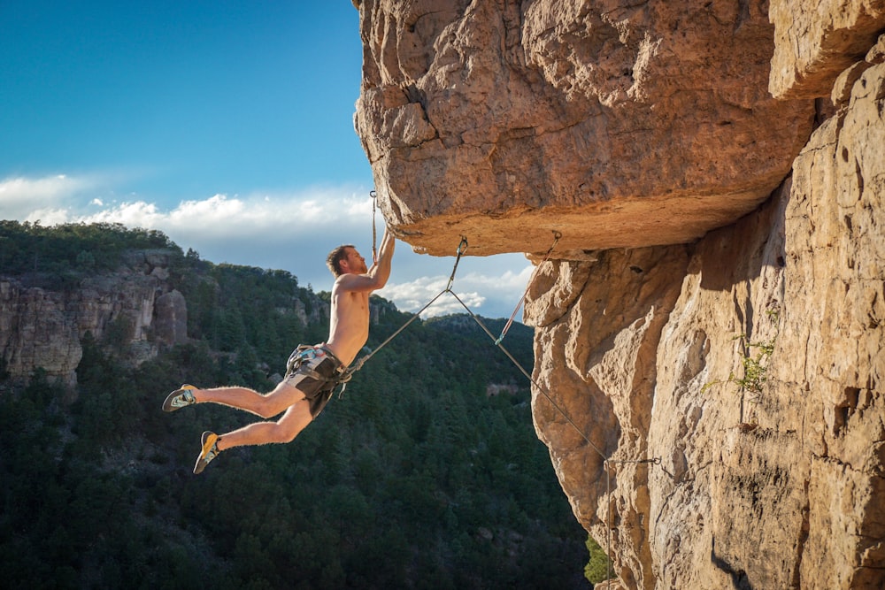 man in black shorts climbing on brown rock formation during daytime