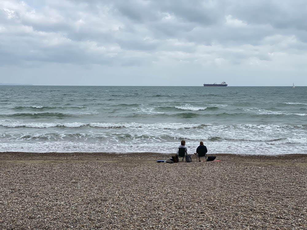 2 people sitting on beach shore during daytime