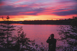 A candid shot of a traveler capturing a sunset over a serene mountain lake.