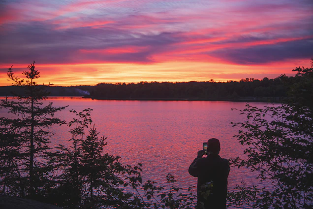 A candid shot of a traveler capturing a sunset over a serene mountain lake.
