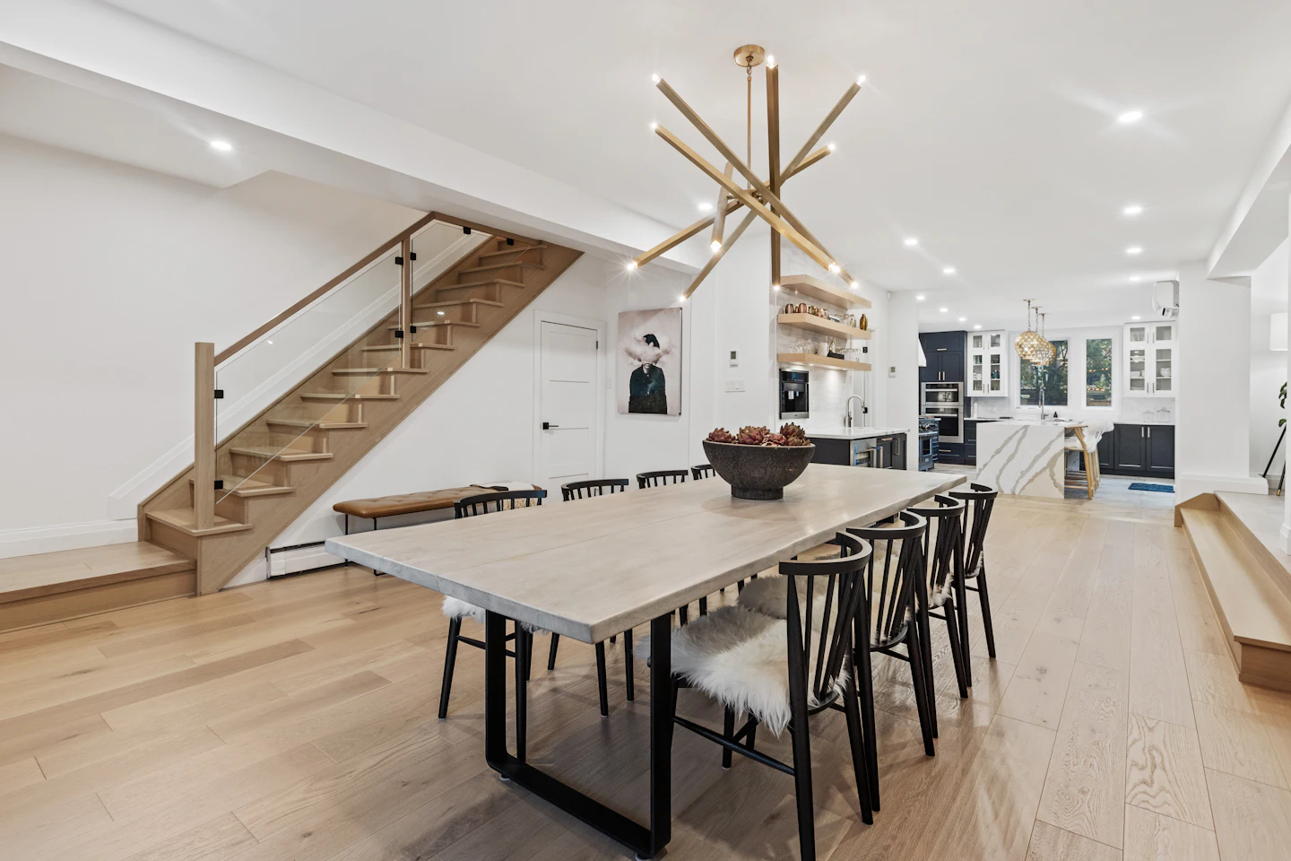 Dining table under a modern light fixture next to a floating staircase