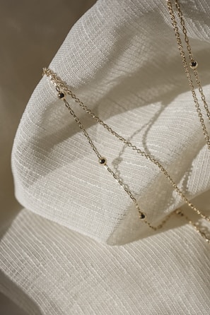 silver necklace on white textile