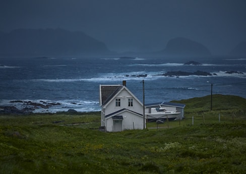 white wooden house on green grass field near body of water during daytime