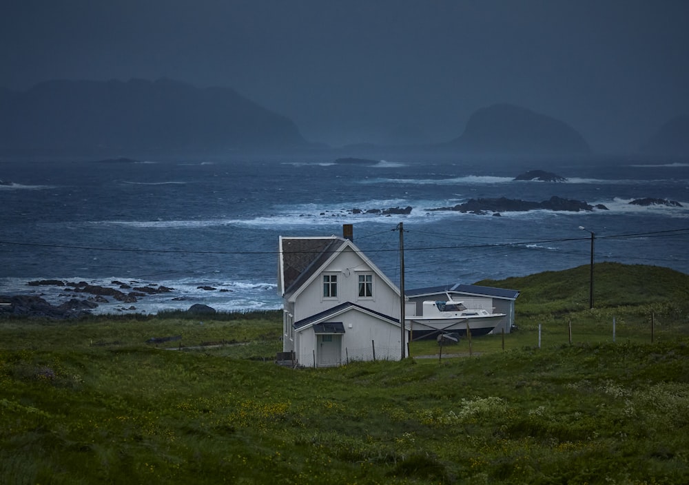 white wooden house on green grass field near body of water during daytime