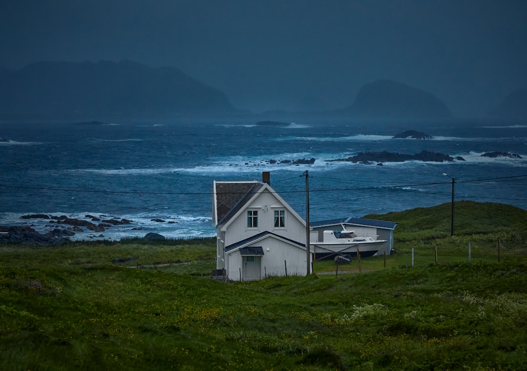 white wooden house on green grass field near body of water during daytime