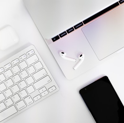 A modern laptop paired with wireless headphones and a portable Bluetooth speaker on a clean white surface.