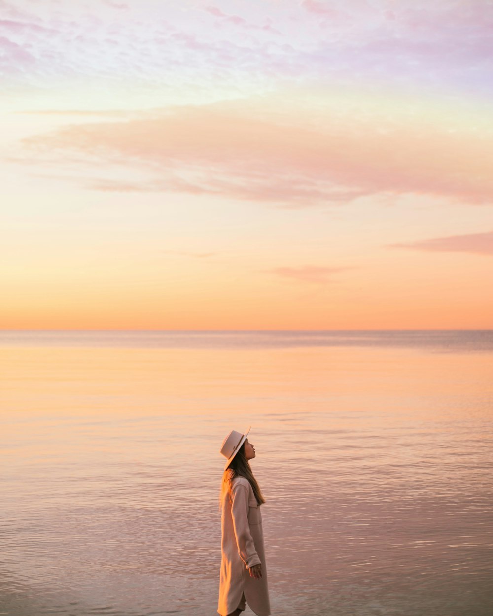 mulher no vestido preto e branco de pé na costa do mar durante o pôr do sol