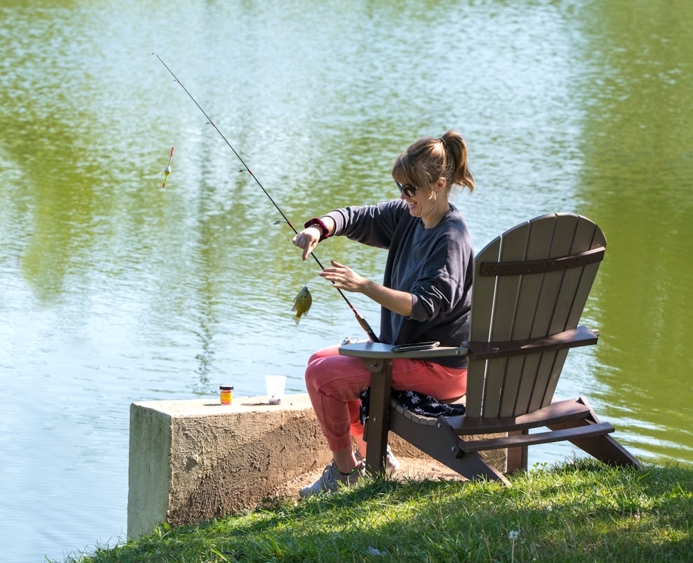 woman in blue shirt and black pants sitting on brown wooden bench while fishing during daytime
