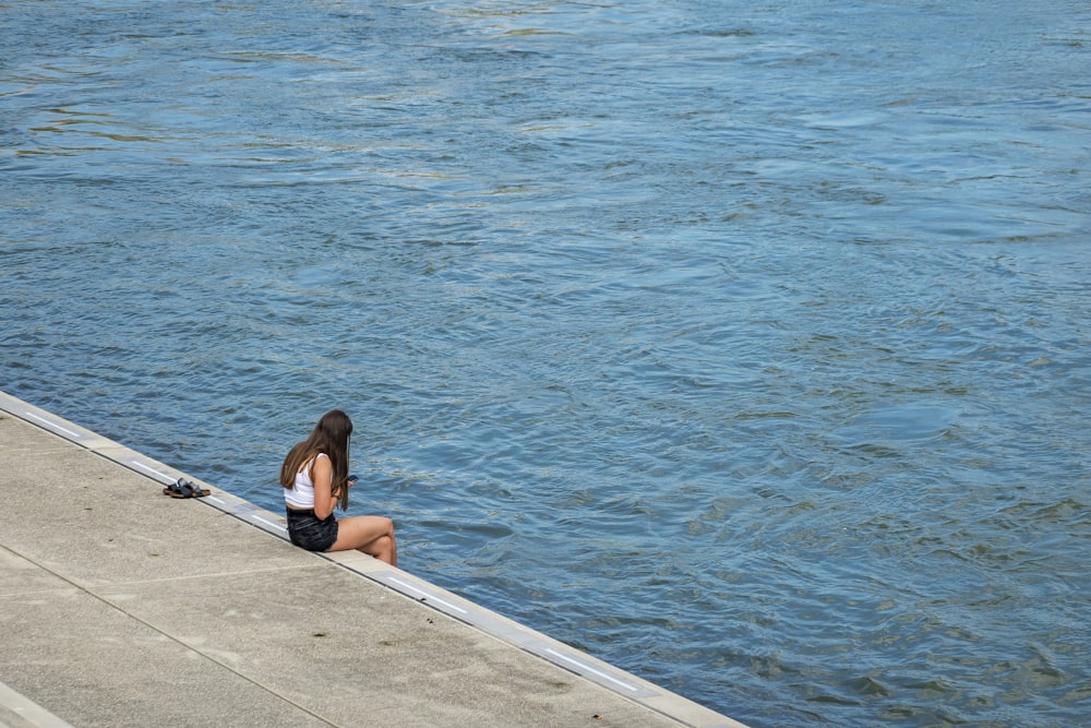 woman in black bikini sitting on dock near body of water during daytime