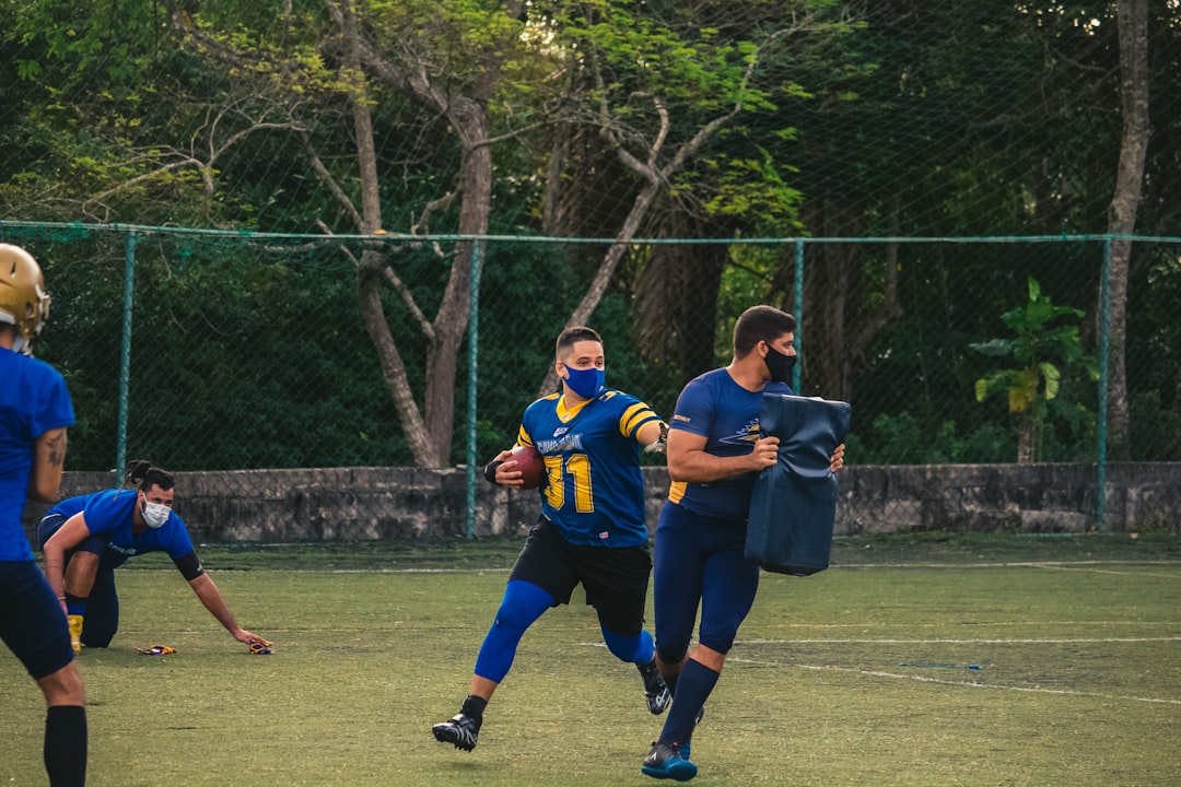 2 men in blue and yellow jersey shirt running on green grass field during daytime