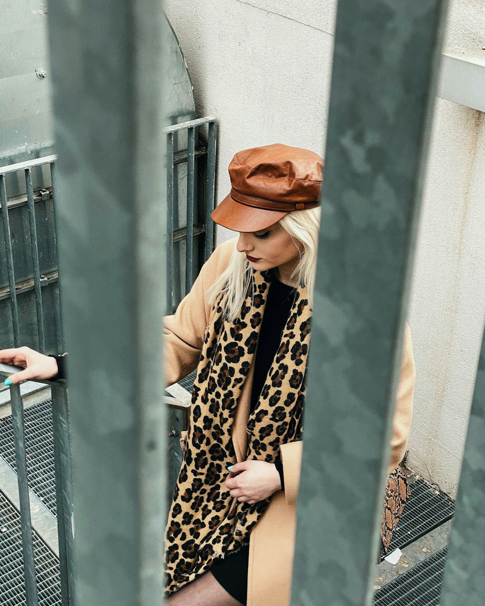 woman in brown coat and leopard print pants standing beside blue wall