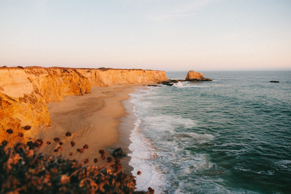 brown rocky mountain beside sea during daytime