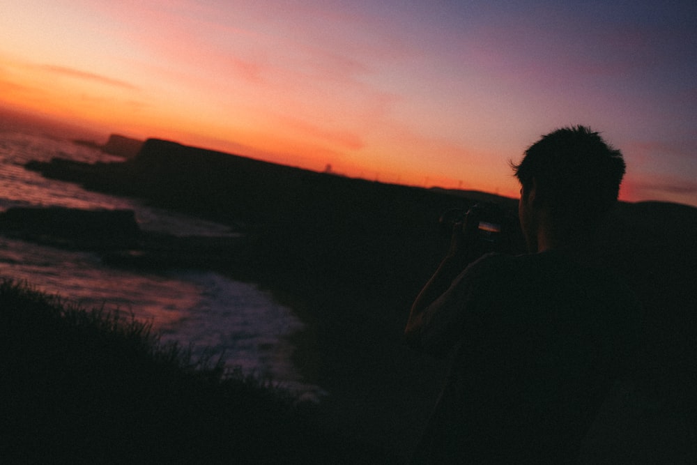 silhouette of man standing near body of water during sunset