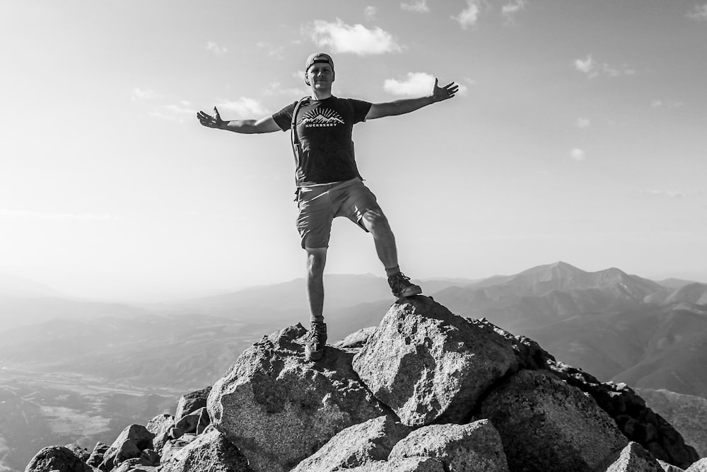 man in black tank top and white shorts standing on rock formation during daytime