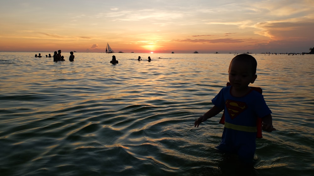 boy in blue and yellow shirt standing on sea water during sunset