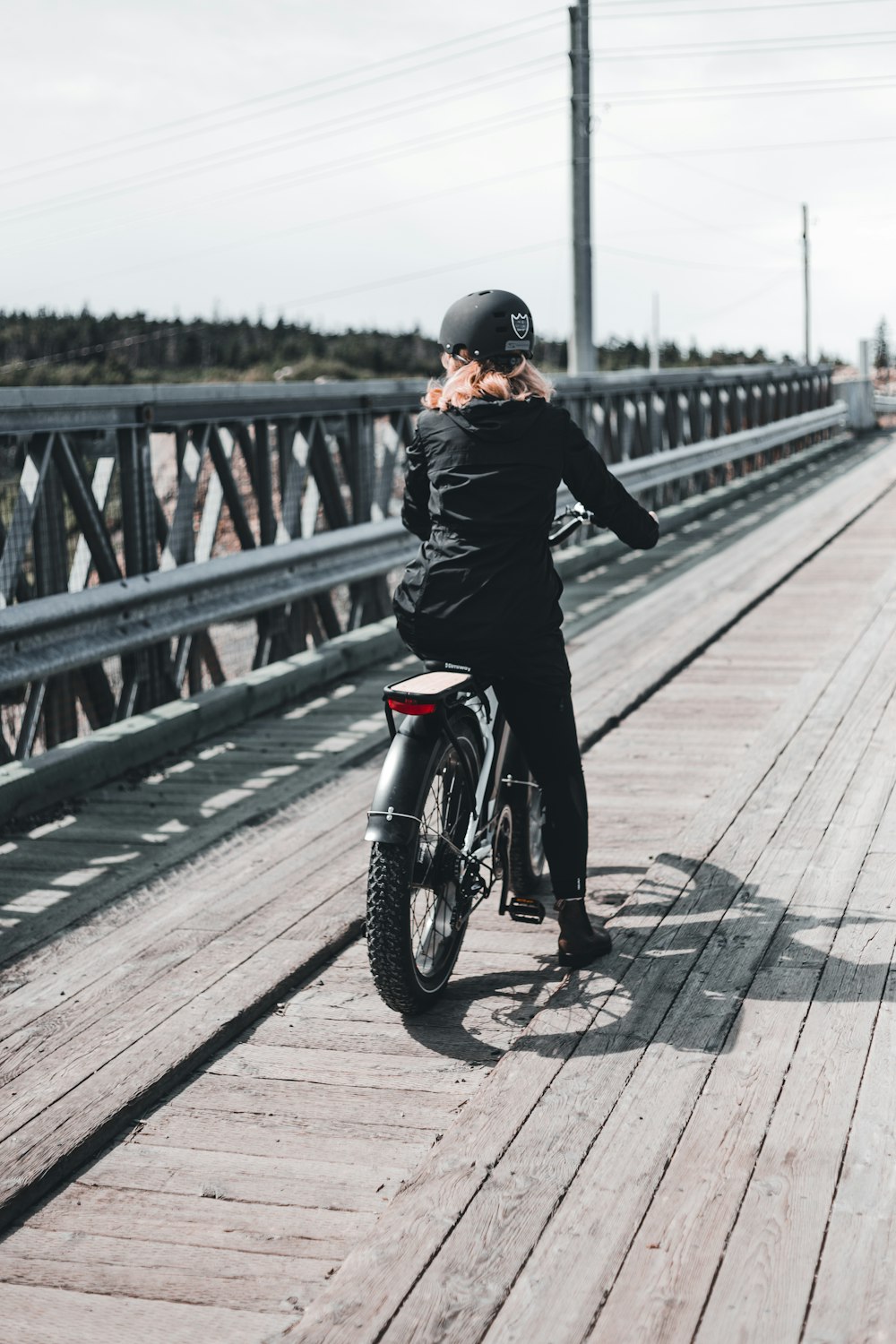 uomo in giacca nera che guida una moto nera sul ponte durante il giorno