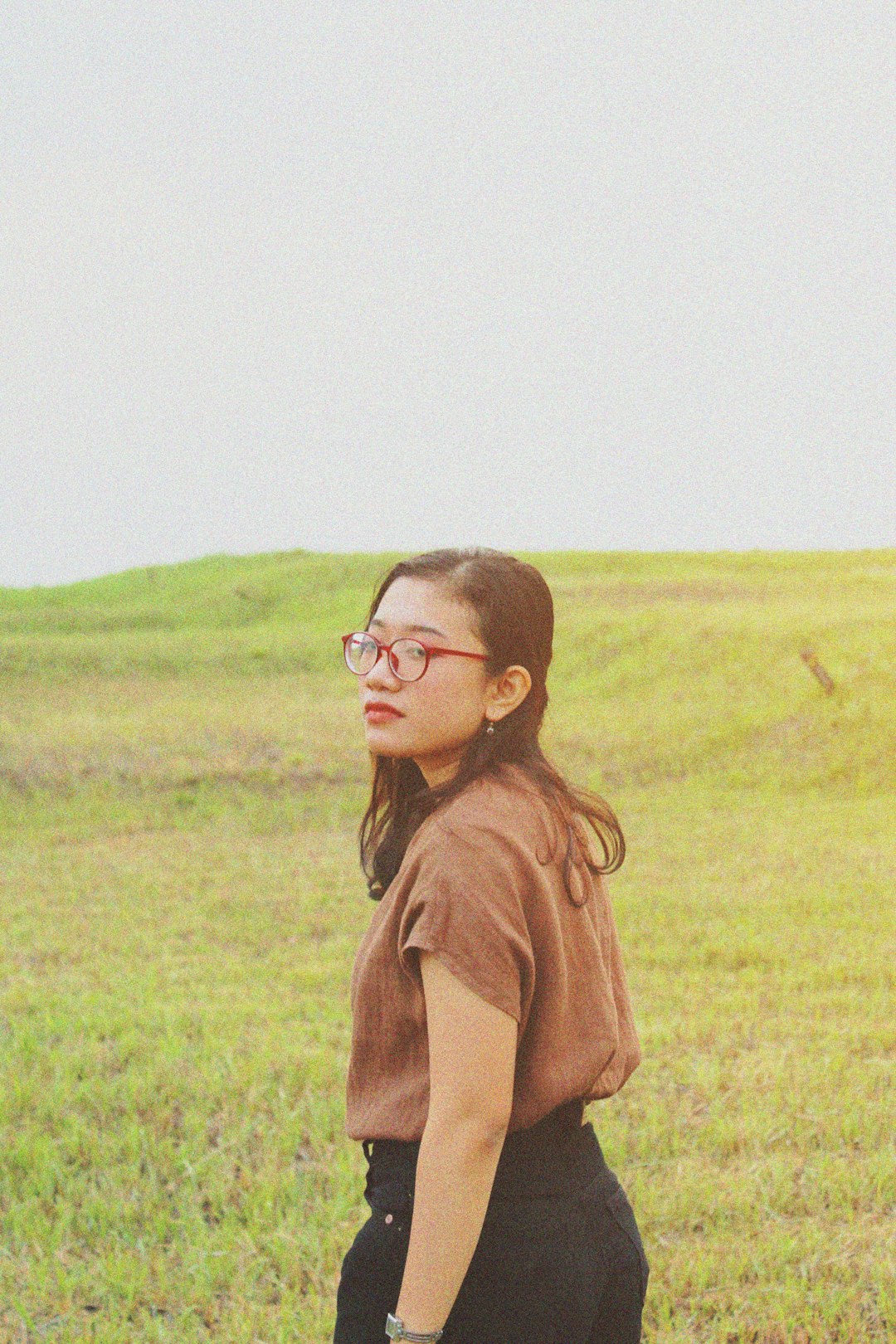 woman in brown long sleeve shirt wearing black framed eyeglasses standing on green grass field during