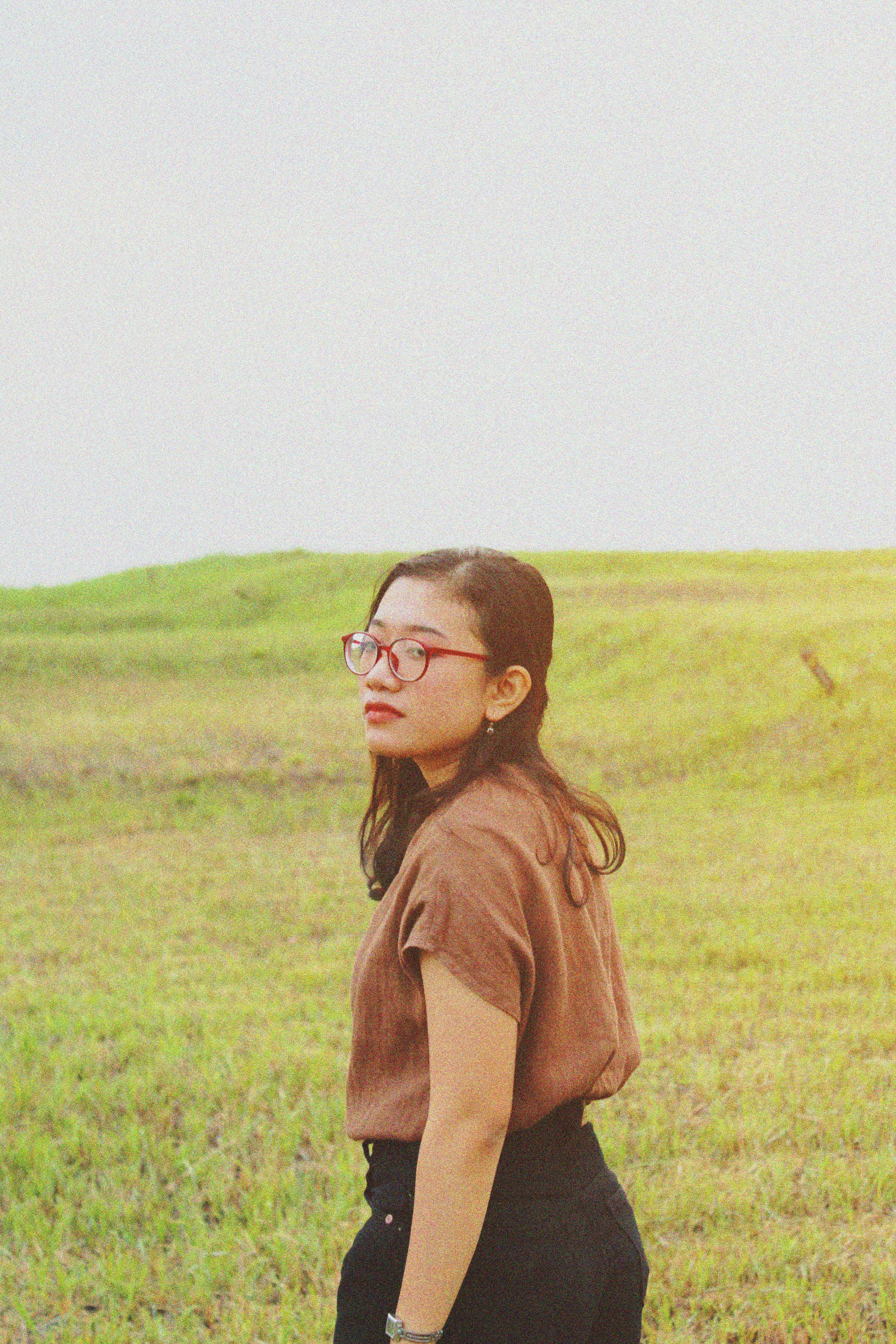 woman in brown long sleeve shirt wearing black framed eyeglasses standing on green grass field during