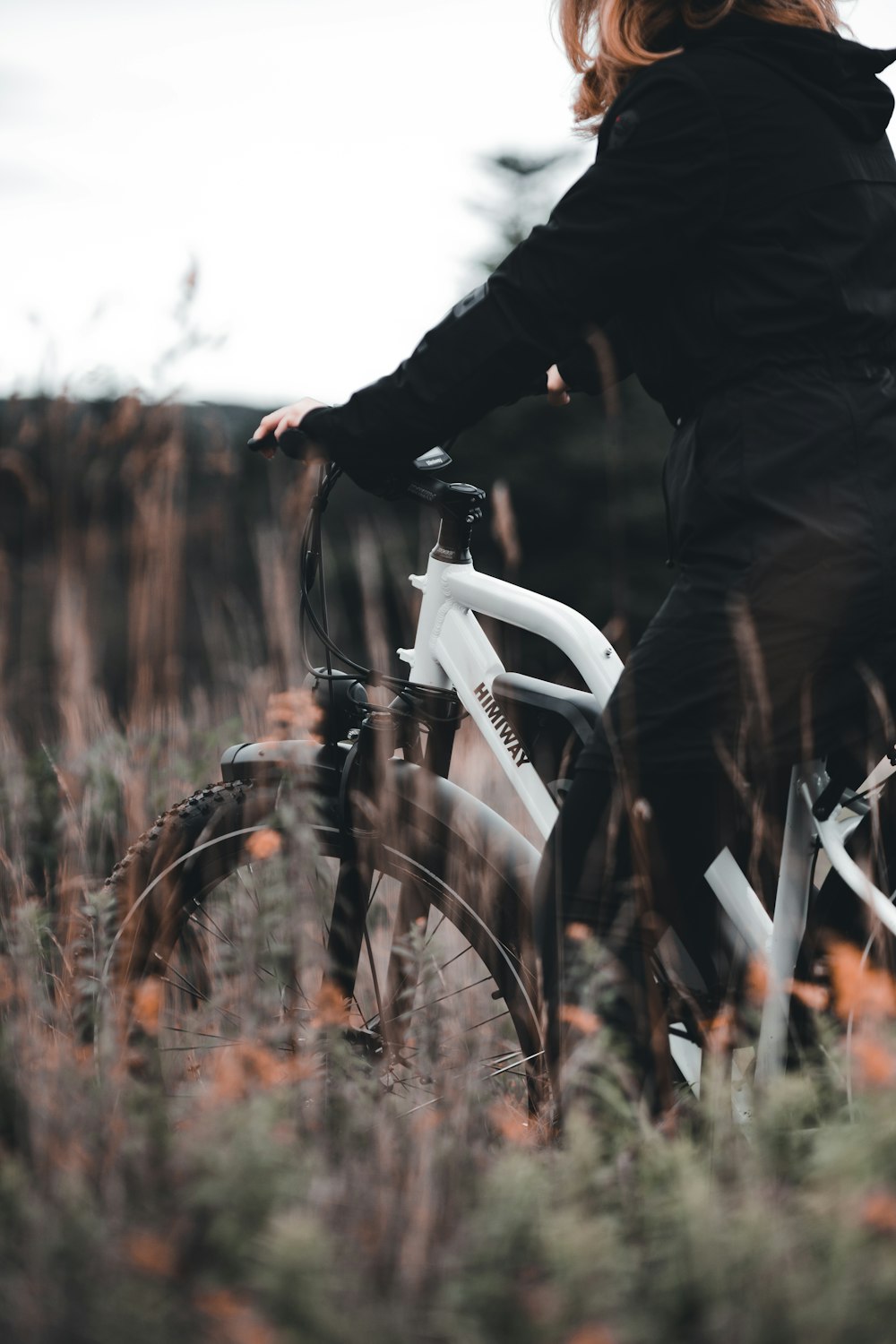 person in black jacket riding white bicycle on brown grass field during daytime