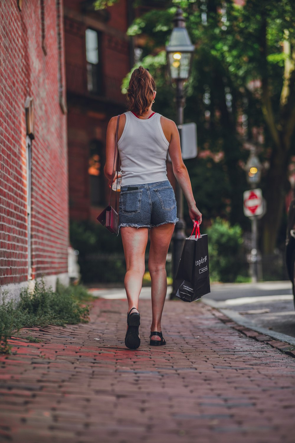 femme en débardeur blanc et short en jean bleu marchant sur le trottoir pendant la journée