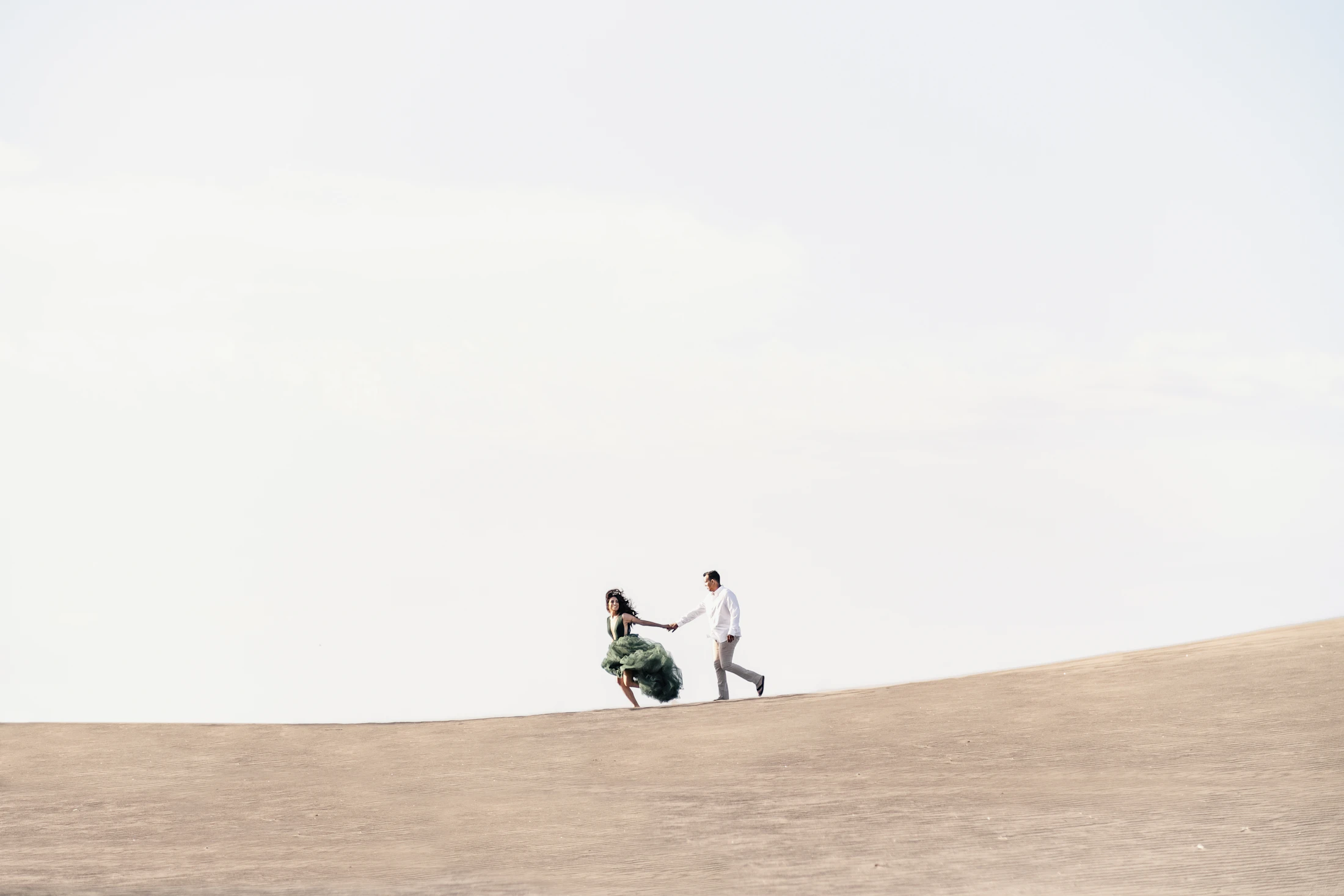 Valeria and Mateo walking hand in hand across a wide sand dune