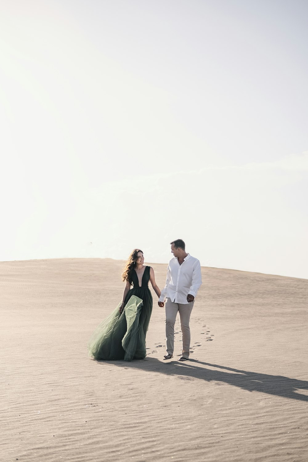 Mann und Frau halten sich Händchen, während sie tagsüber auf braunem Sand spazieren gehen