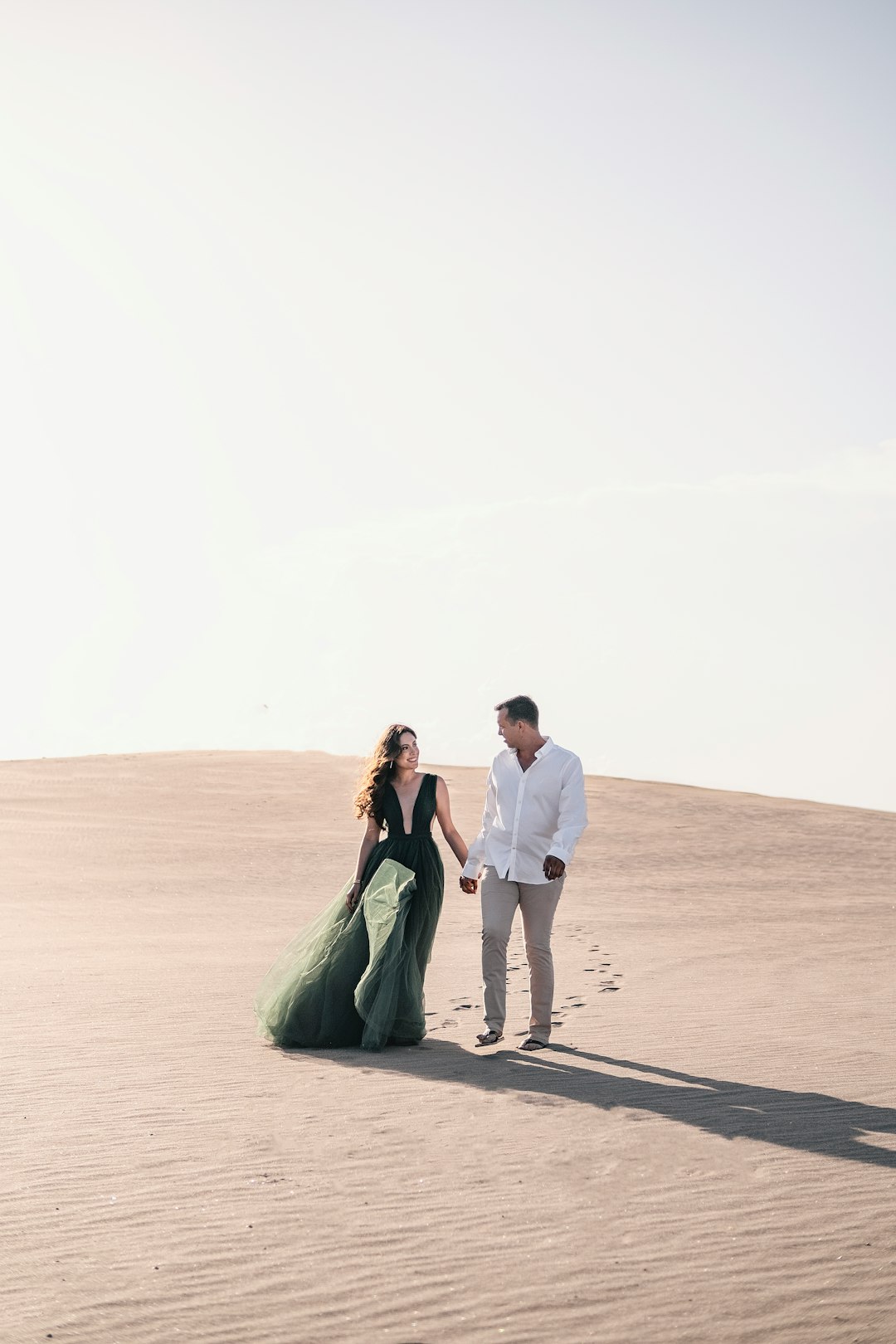 man and woman holding hands while walking on brown sand during daytime