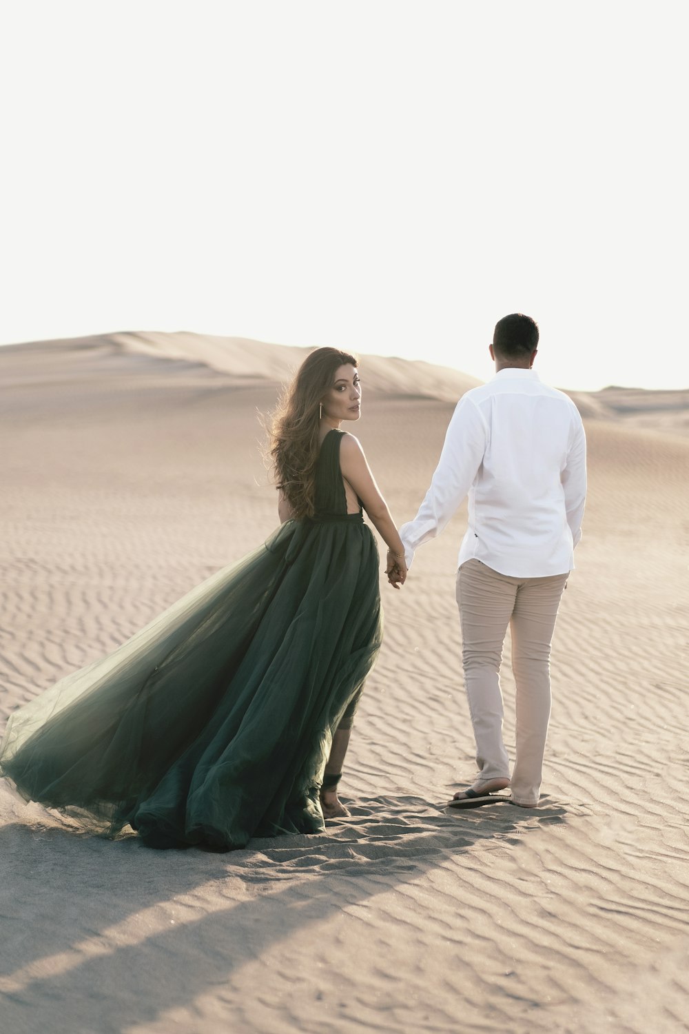 Hombre y mujer tomados de la mano mientras caminan sobre la arena durante el día