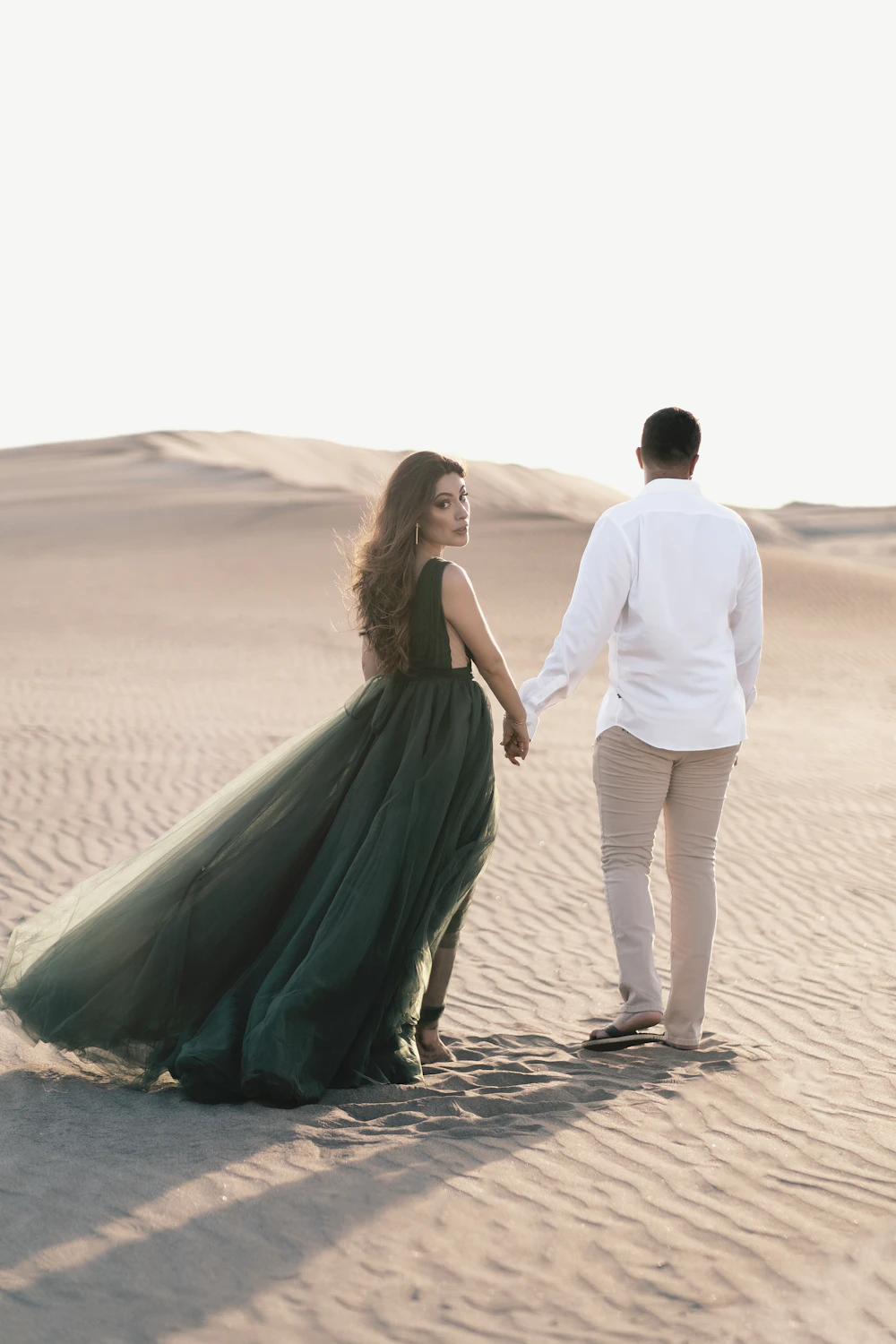 Valeria in an emerald gown looking back while holding Mateo's hand