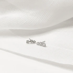 Close-up of delicate minimalist Korean earrings resting on a soft fabric background.