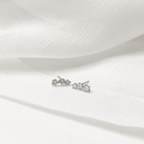 flat lay of modern cubic zirconia silver earrings on soft ivory silk background