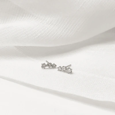 Delicate gold earrings with tiny gemstones sparkling against a white marble background.