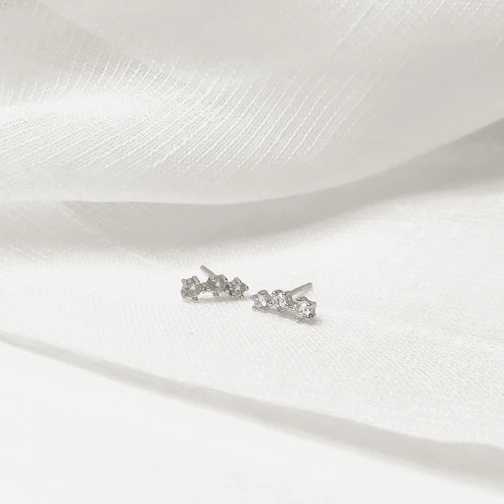 Delicate silver stud earrings on a white marble background emphasizing minimalist elegance.