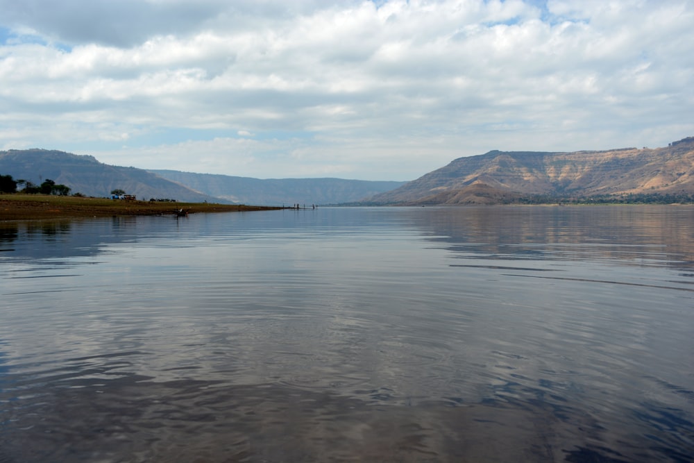 body of water near mountain under white clouds during daytime