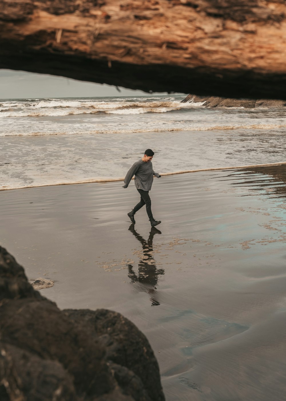 회색 재킷과 검은 바지를 입은 남자가 낮 동안 해변을 걷고 있다