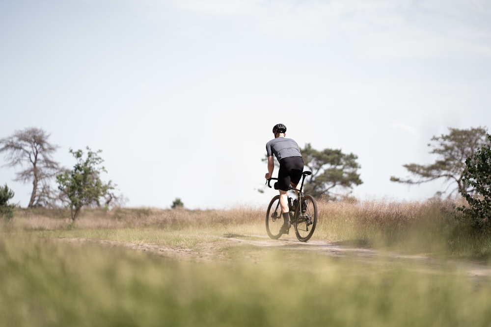 man in black jacket riding bicycle on green grass field during daytime