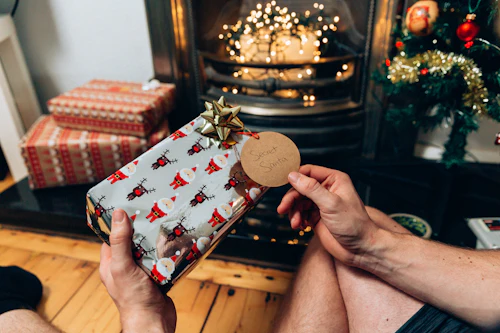 Deux personnes s'échangent un cadeau emballé près d'une cheminée décorée pour Noël