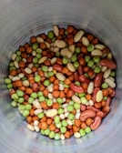 A collection of mixed nuts and seeds with various colors including green, brown, and beige arranged inside a metallic container.