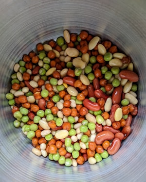 A collection of mixed nuts and seeds with various colors including green, brown, and beige arranged inside a metallic container.
