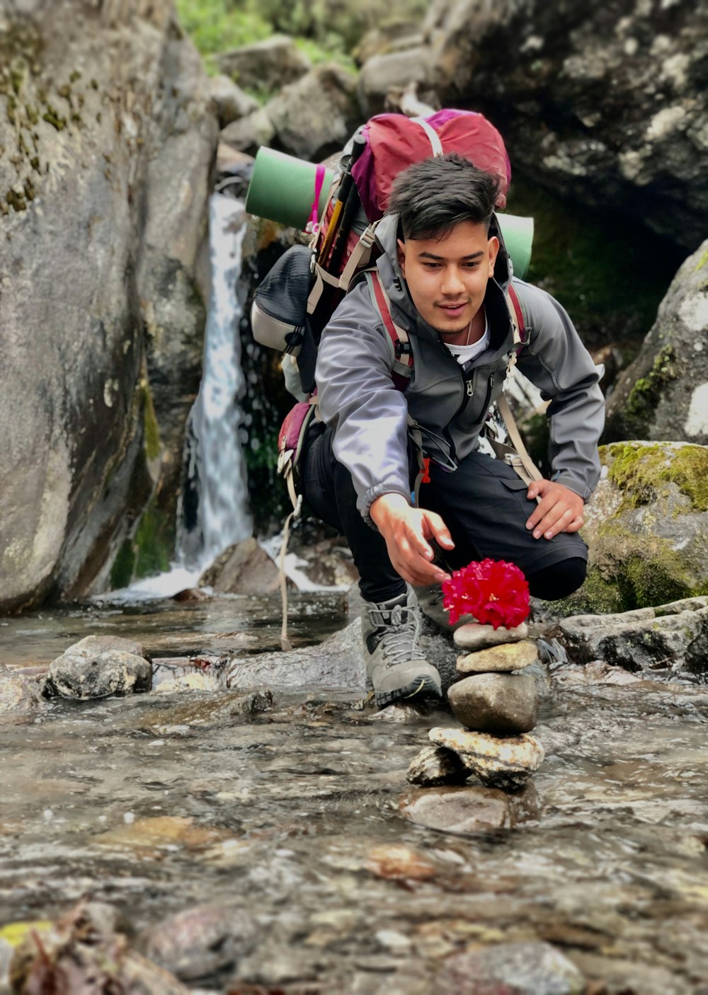 man in black jacket and red pants sitting on rock