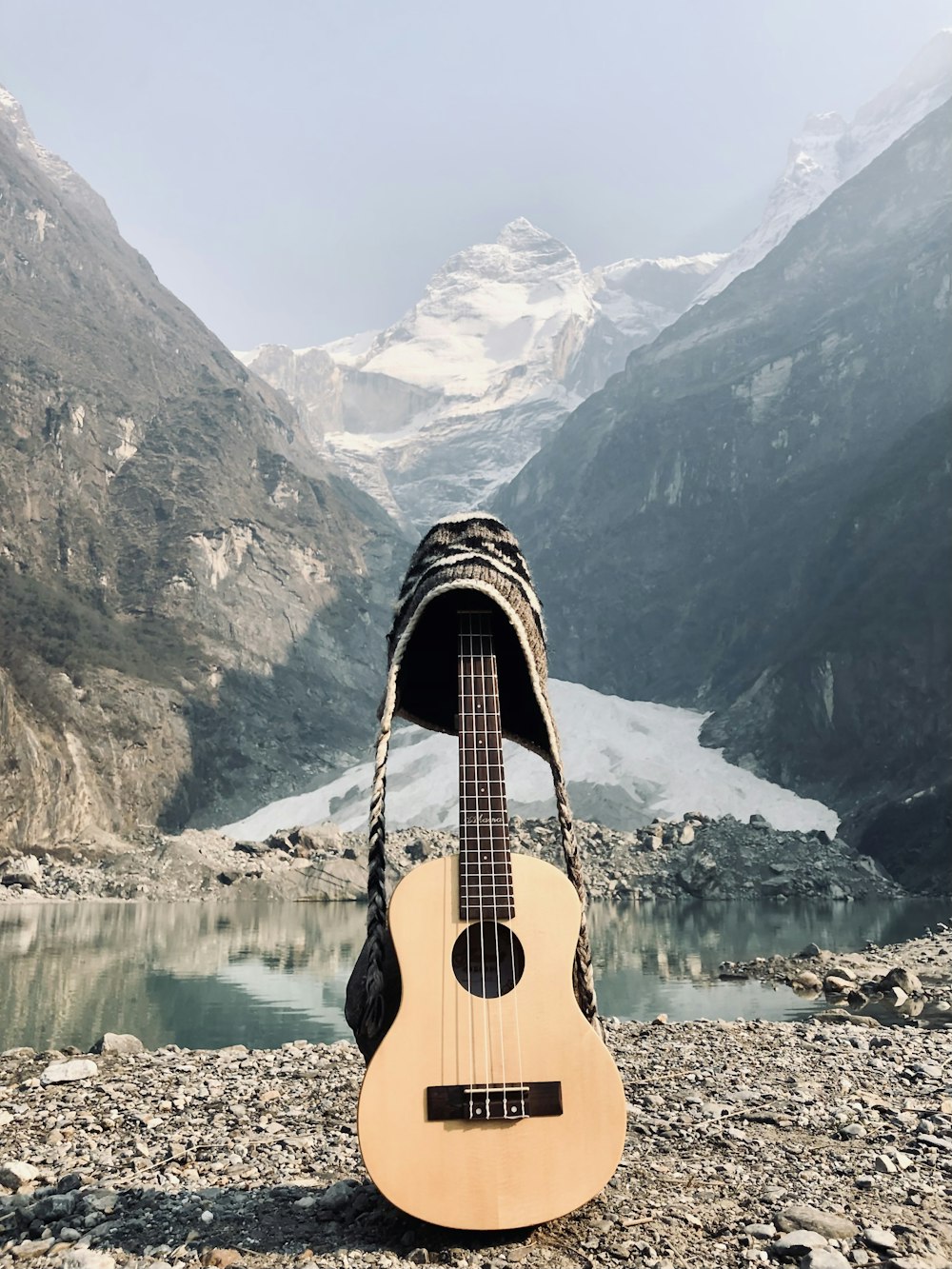 guitarra acústica marrom na doca de madeira marrom perto do lago e da montanha coberta de neve durante o dia