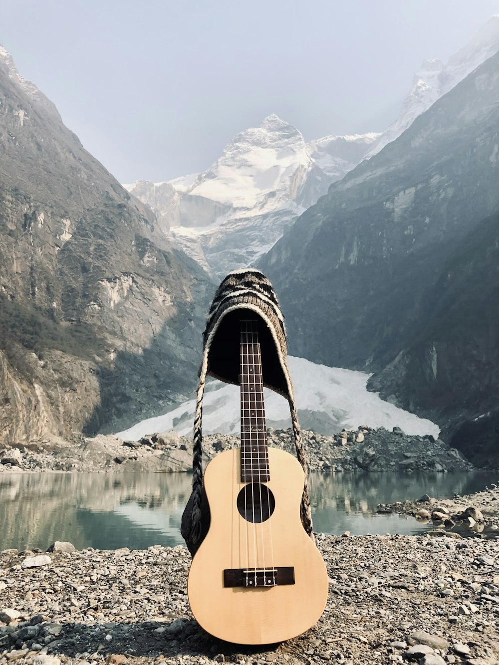 Guitarra acústica marrón en muelle de madera marrón cerca del lago y la montaña cubierta de nieve durante el día