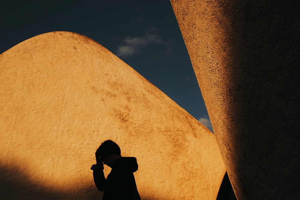 man in black jacket and black cap standing beside brown concrete wall during daytime